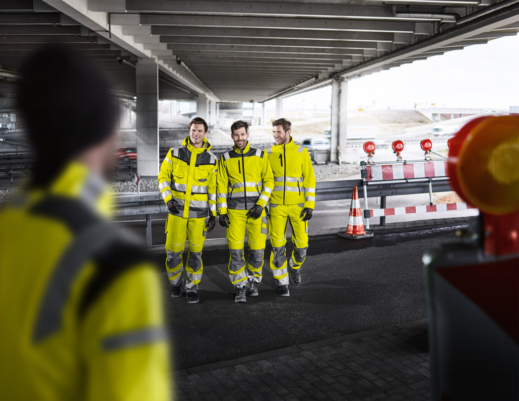 vier Männer in Warnschutzkleidung unter Autobahnbrücke auf Baustelle